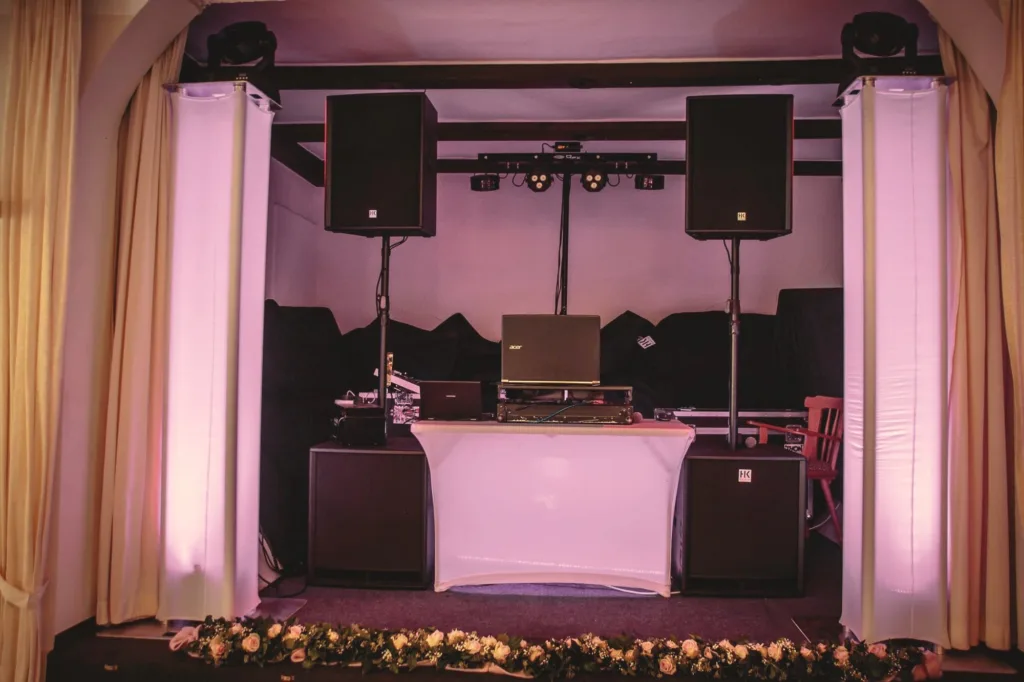 DJ-Aufbau auf einer Bühne mit beleuchteten Säulen und Blumenschmuck