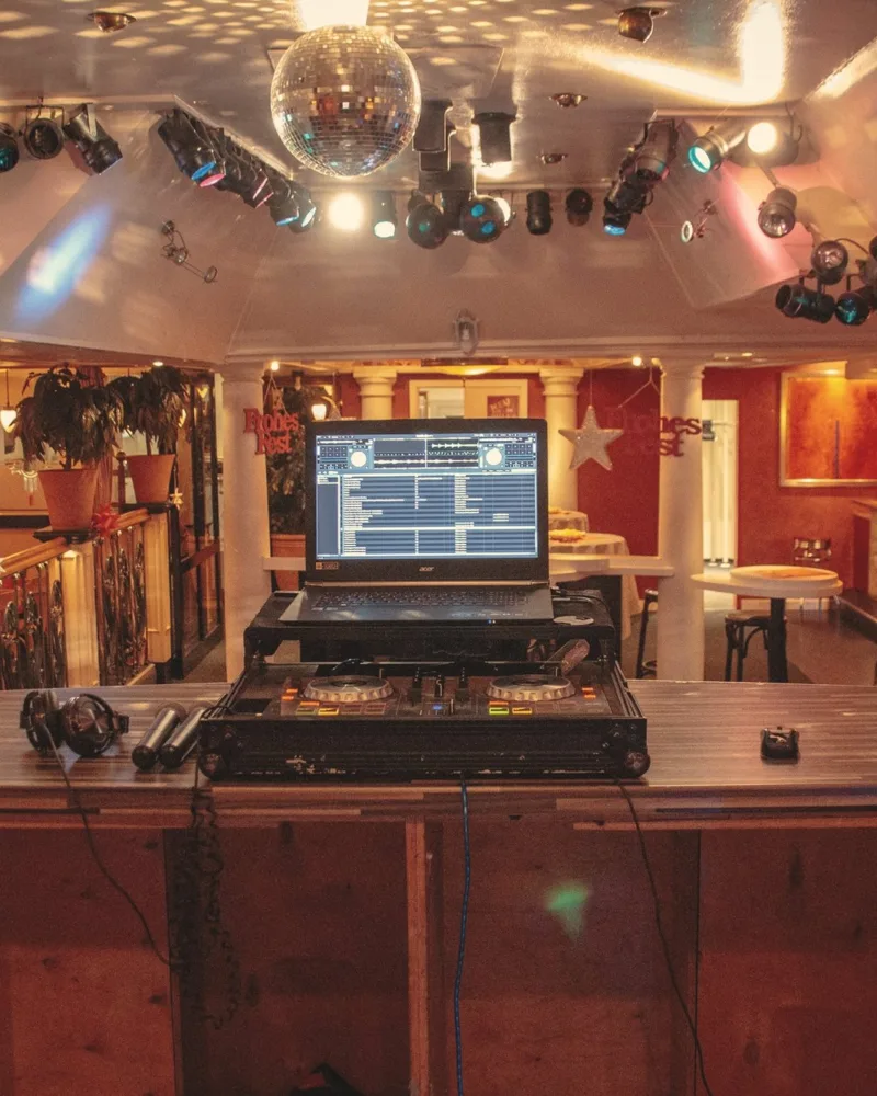 DJ-Pult mit Laptop unter Discokugel und Scheinwerfern in einer Partylocation