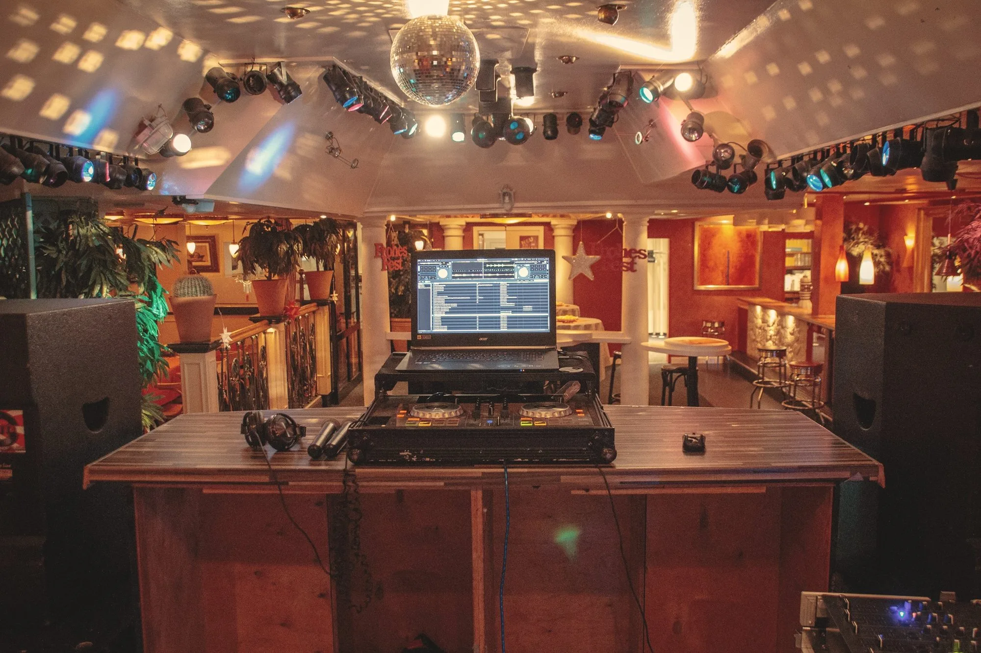 DJ-Pult mit Laptop unter Discokugel und Scheinwerfern in einer Partylocation